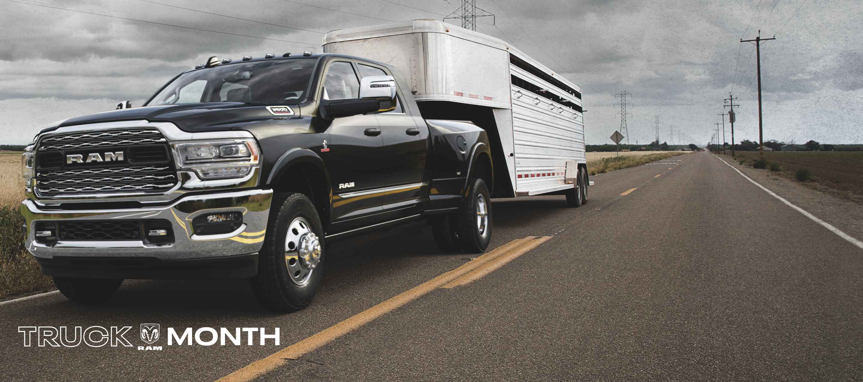 A black 2024 Ram 3500 Limited Mega Cab towing a fifth wheel travel trailer as it is driven down the highway. Truck Month Sales Event.