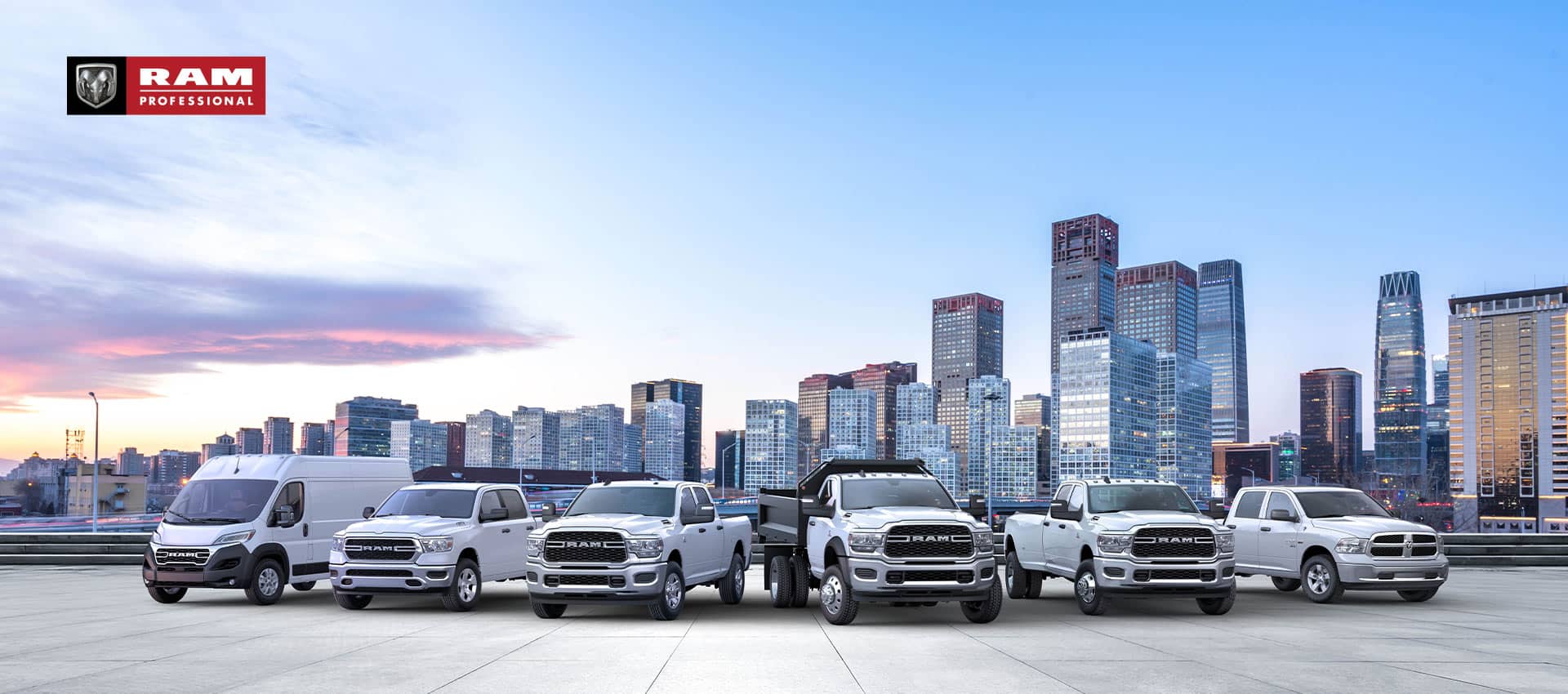 The Ram Brand lineup, all in white, parked side-by-side with a cityscape at dusk in the background. Beginning on the left: a 2024 Ram ProMaster 3500 High Roof Cargo Van, 2024 Ram 1500 Tradesman Crew Cab, 2024 Ram 2500 Tradesman Crew Cab, 2024 Ram 5500 Tradesman Regular Cab with dump body, 2024 Ram 3500 Tradesman Crew Cab and 2024 Ram 1500 Classic Tradesman Crew Cab. Ram Professional.